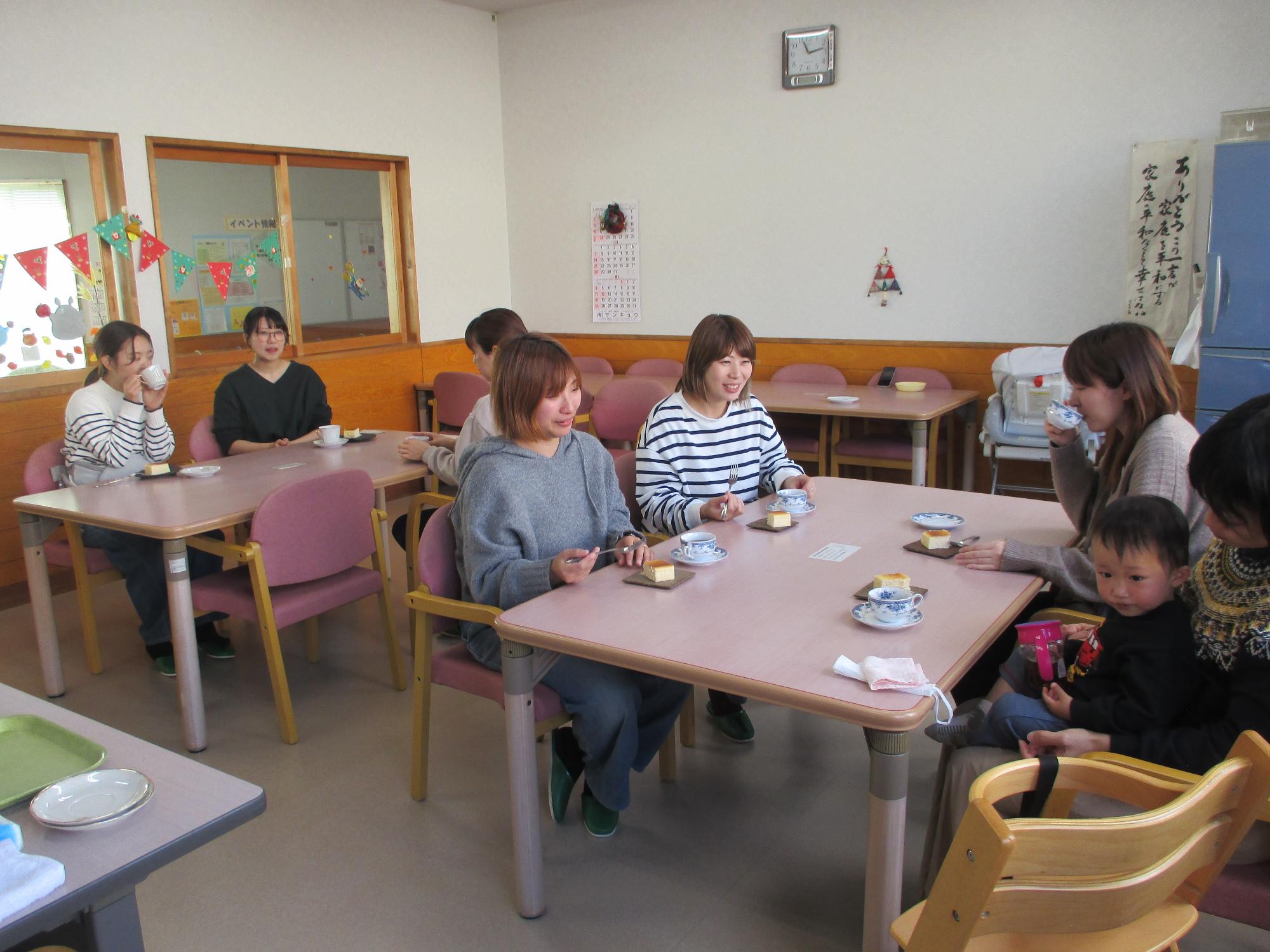 2代のテーブルを囲んで7人の女性がティータイムを楽しんでいる机上にはコーヒーとチーズケーキ