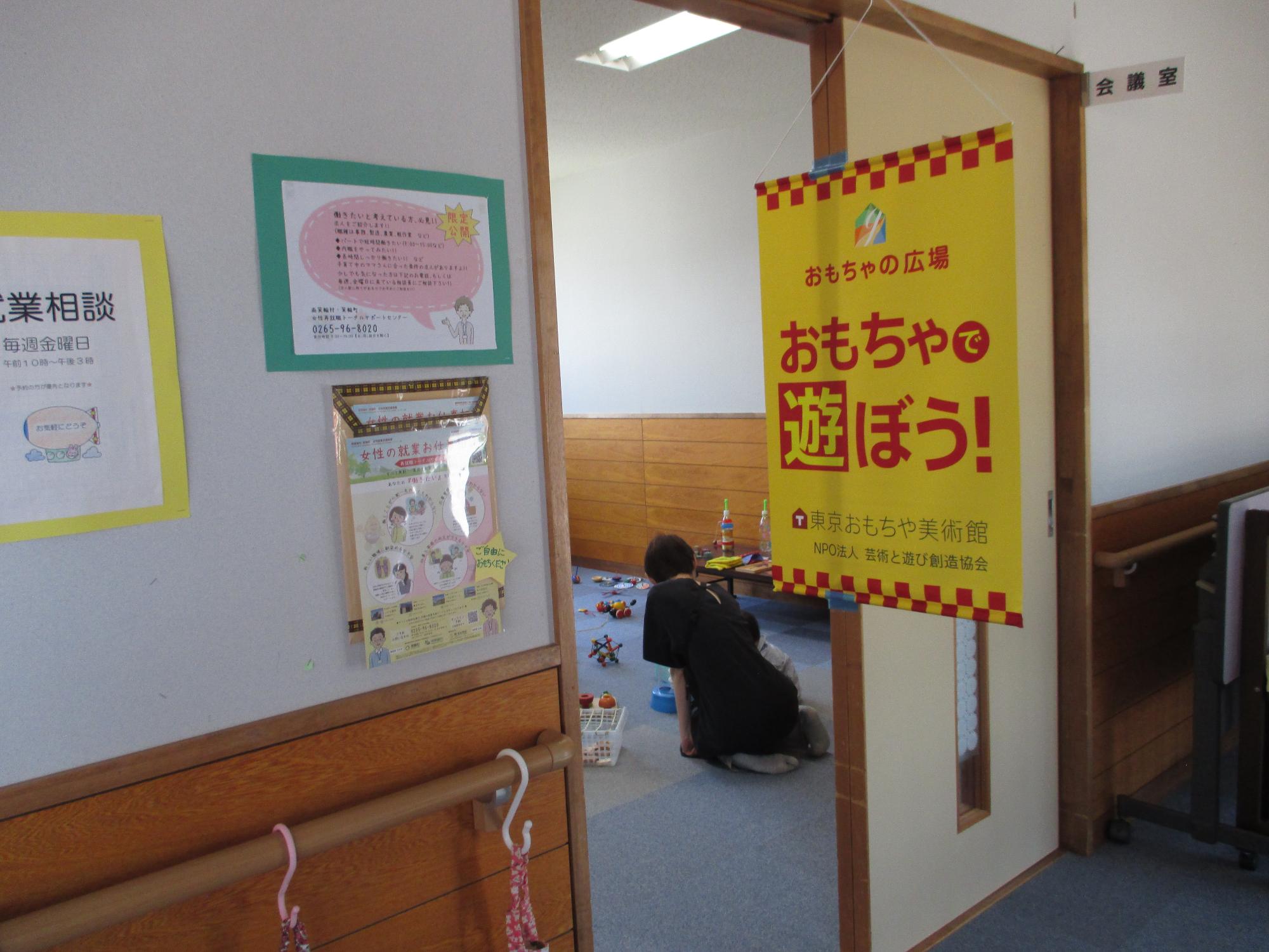おもちゃの広場 おもちゃで遊ぼうと書かれた看板がありおもちゃが置かれた部屋が見える