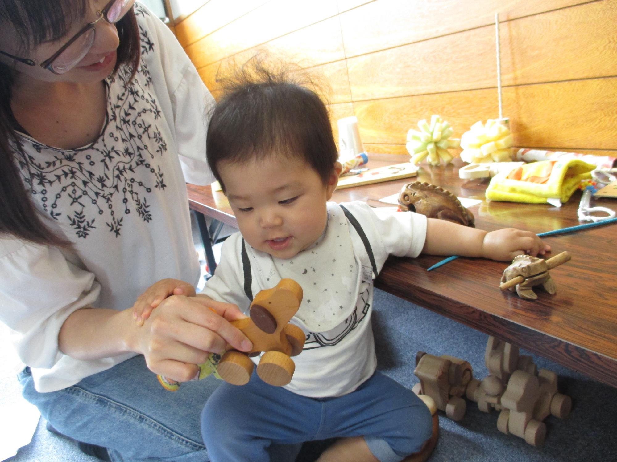 母の膝の上で木の犬のおもちゃをみている0歳児