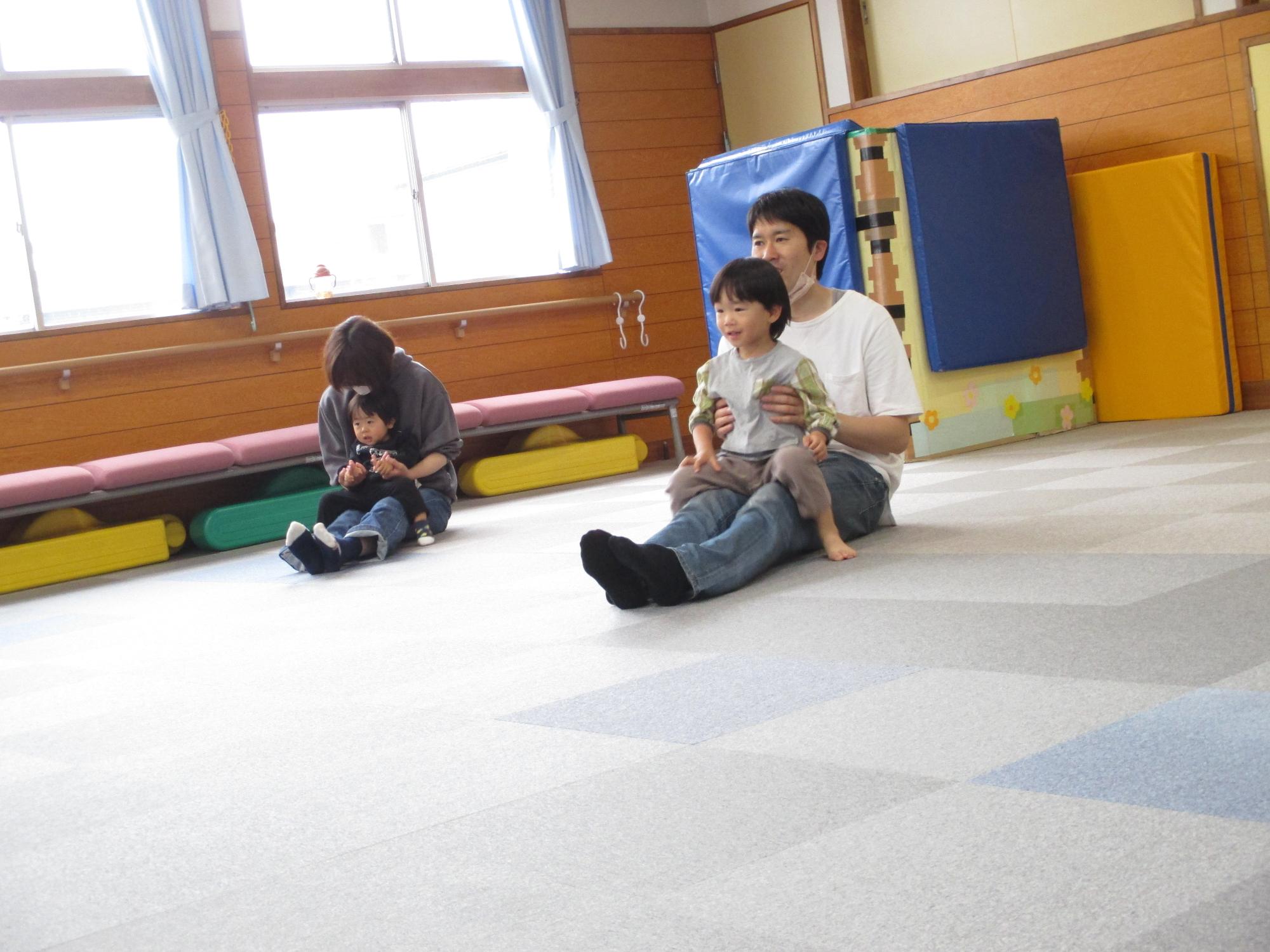 父と子、母と子で2組、親の膝の上に子どもを載せてバスに乗って、の曲に合わせて楽しんでいる