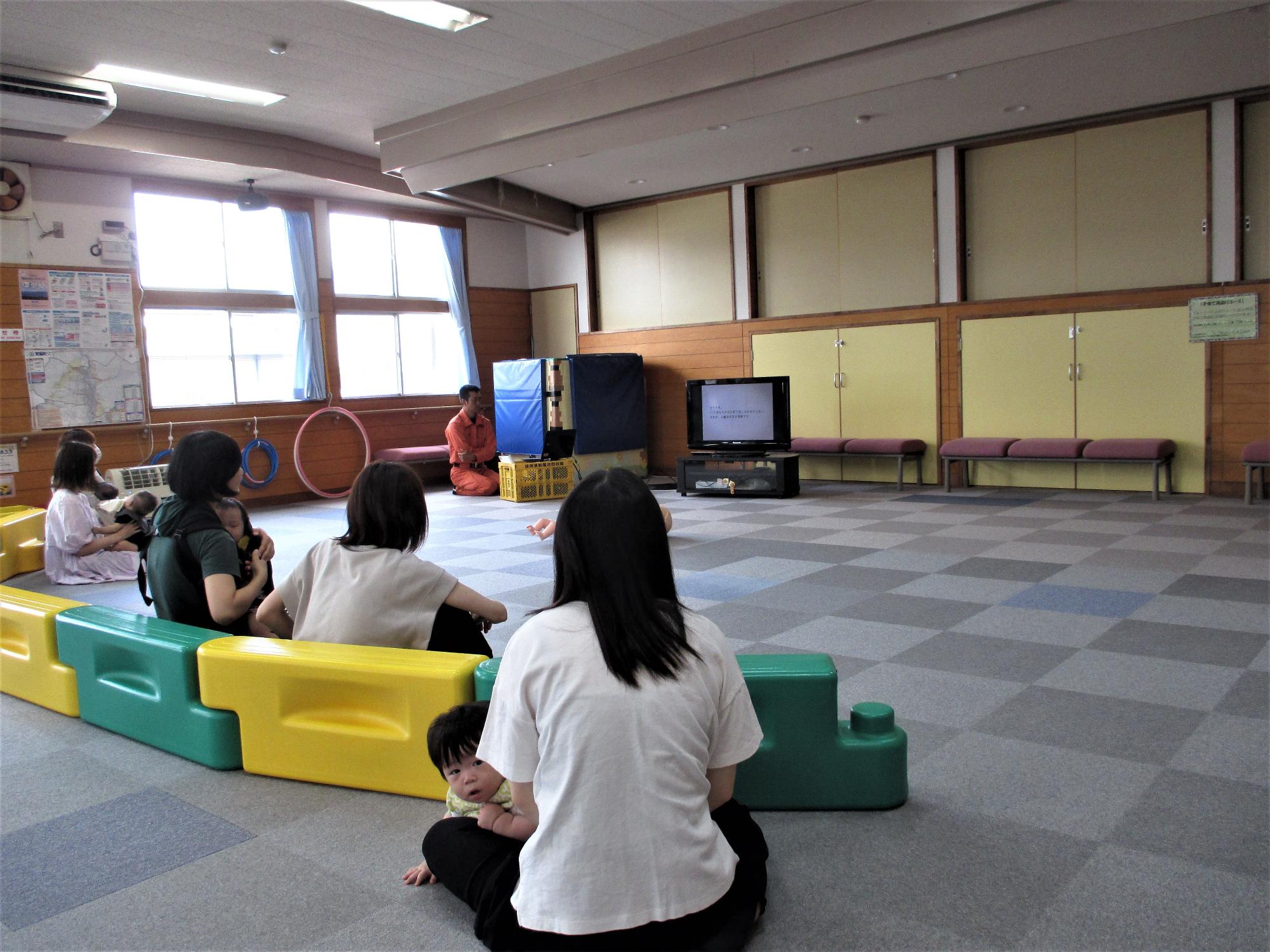救急事例をテレビ画面で見ている母親の座っている後ろ姿
