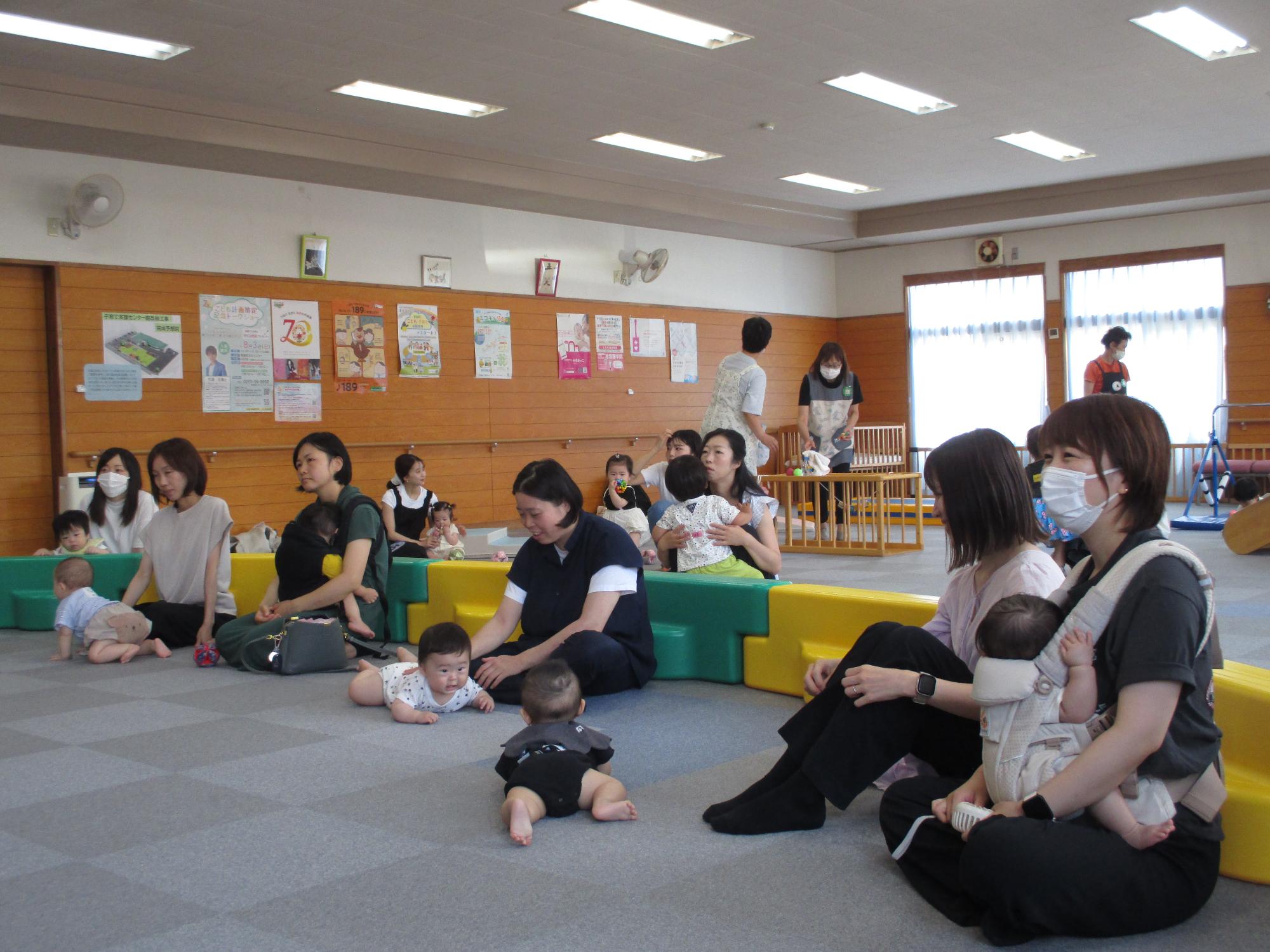 0歳児を抱っこしたりひざ元において講師の話を聞いている母親