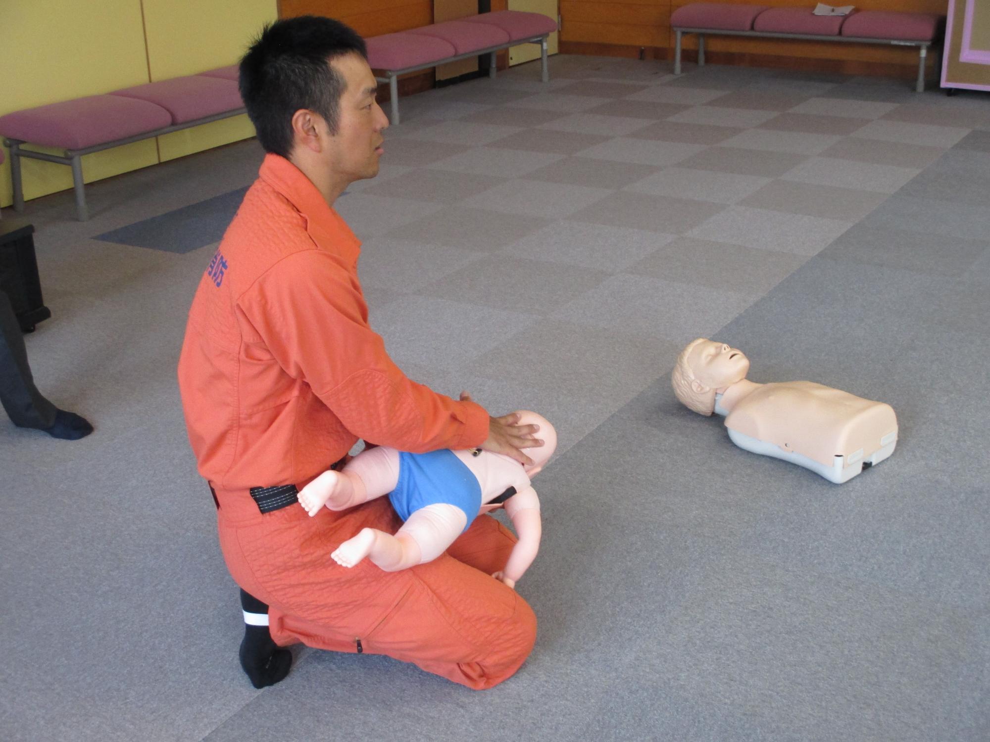 赤ちゃんの人形を抱えて背部工打法の見本を見せる救急救命士