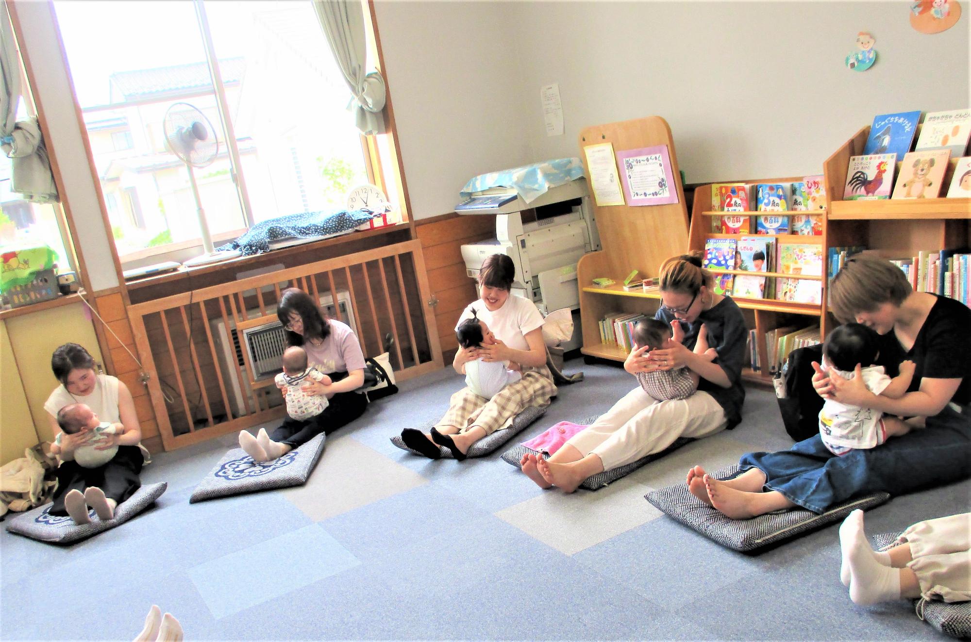 伸ばした膝の上に1歳未満の子どもを載せて向かい合っている母子5組