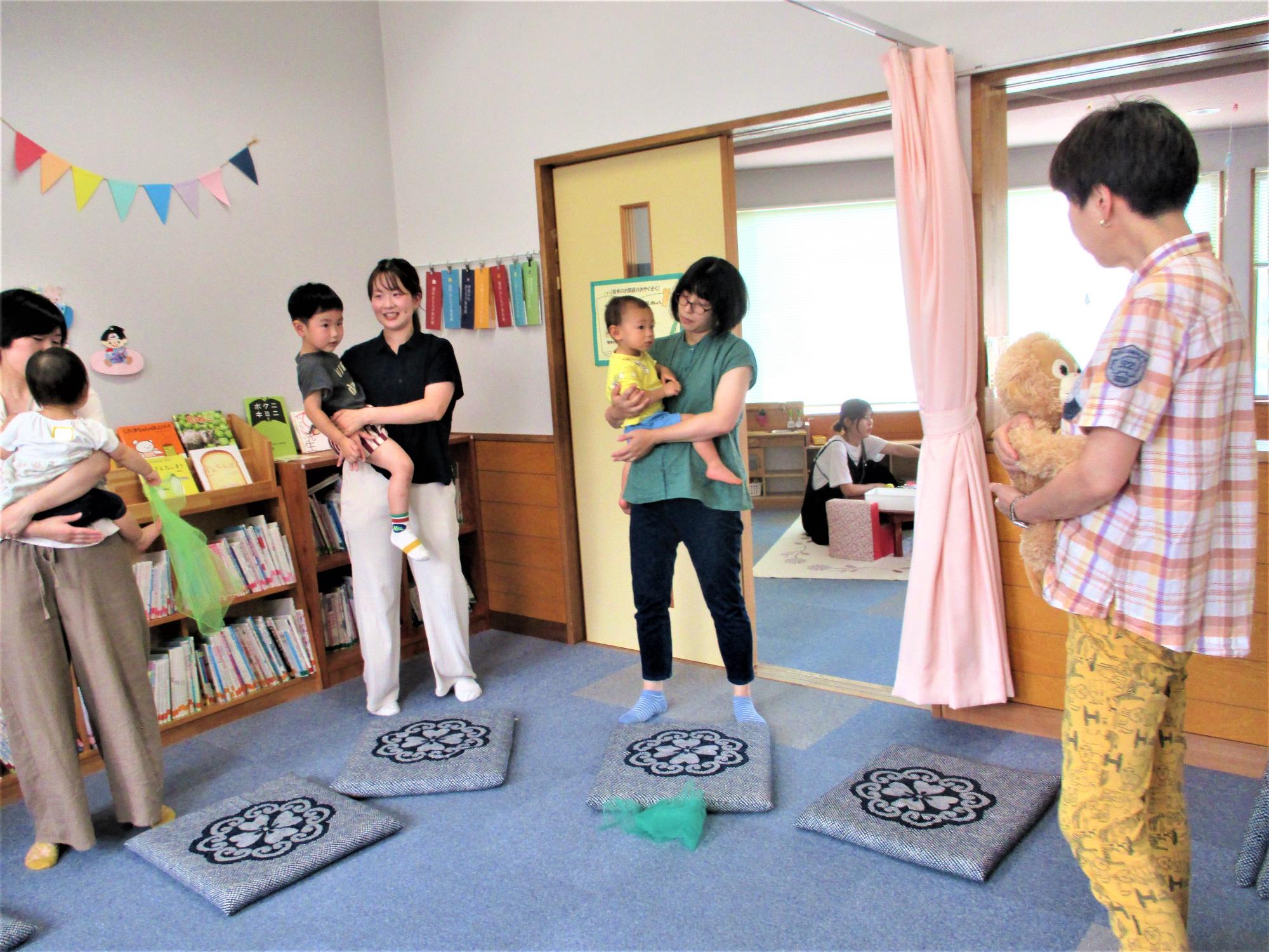 1歳児を抱っこしている3人の母と講師はクマのぬいぐるみを抱っこしている立ち姿