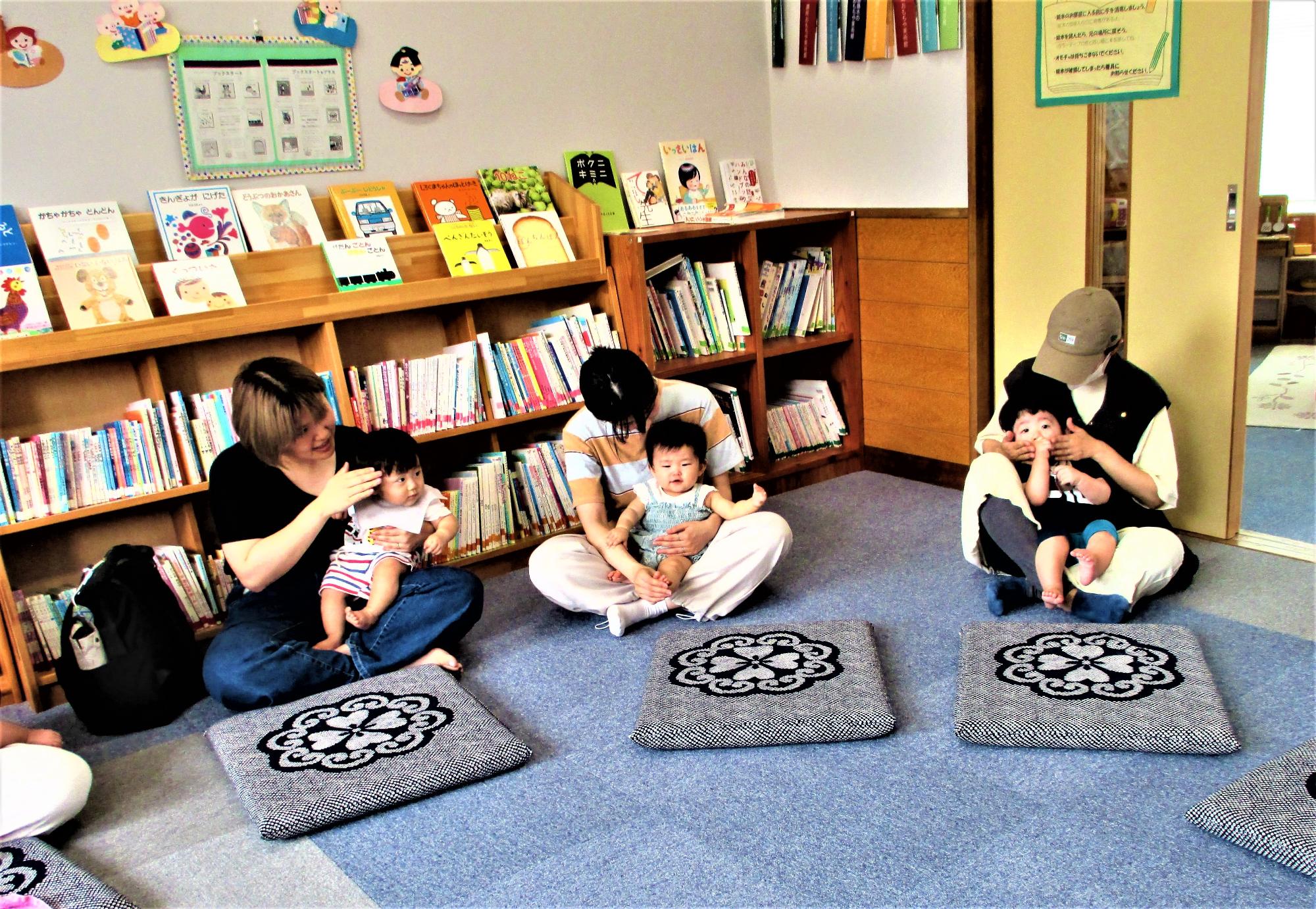 1歳未満の我が子を膝の載せて顔や頭をなぜながら子どもを見つめている母3人