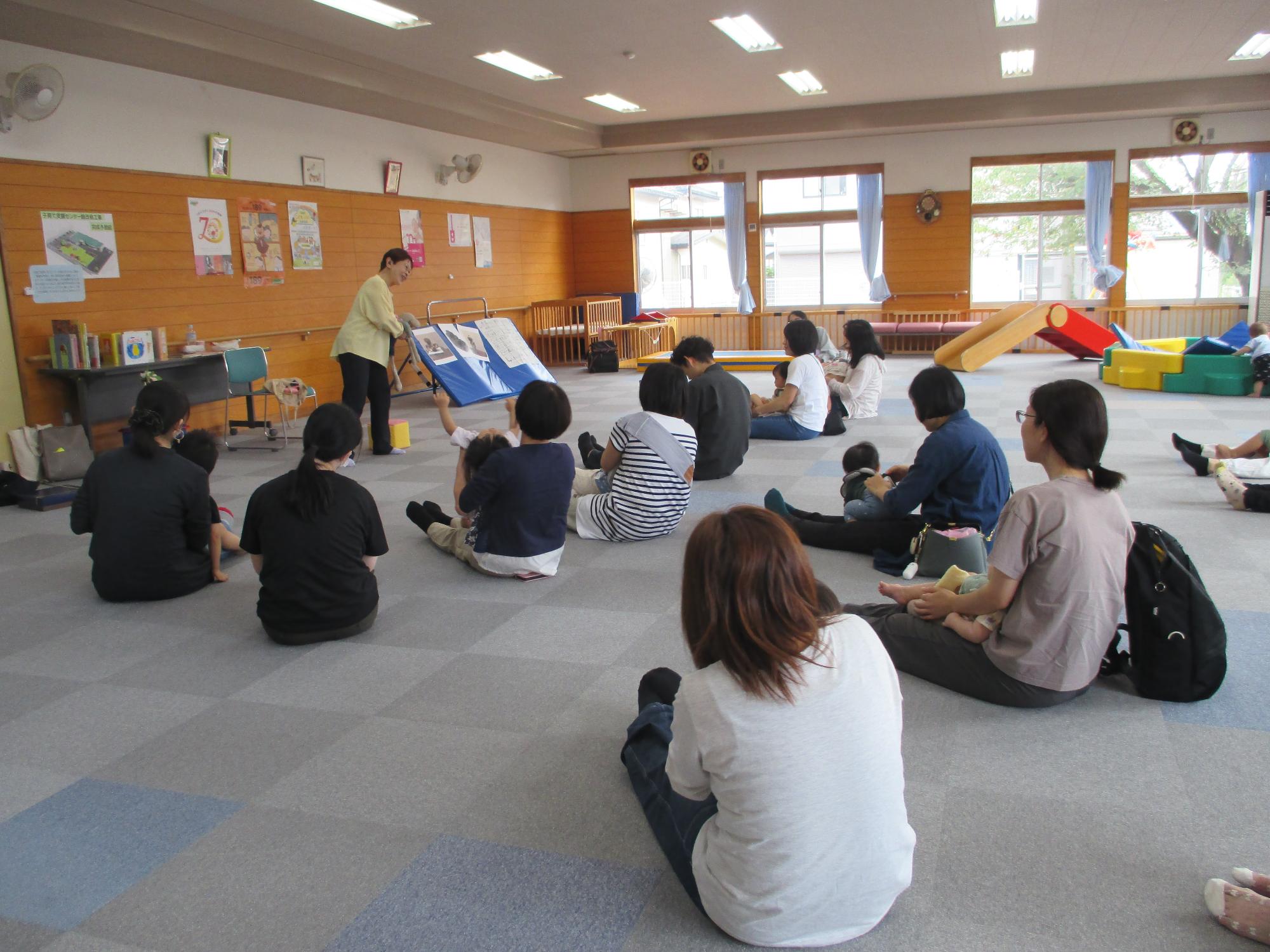 立っている講師を大勢の親子が床に座り見ている。