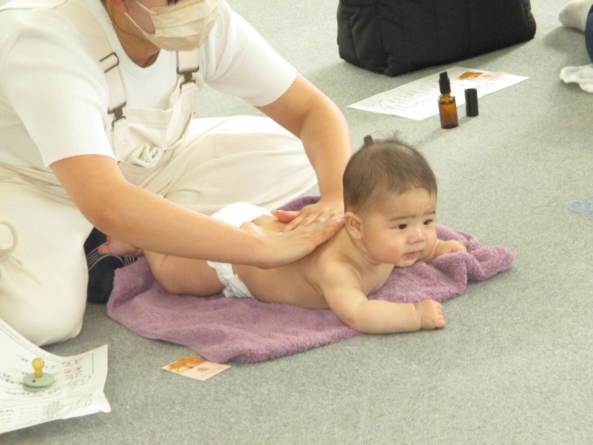 裸でうつぶせの赤ちゃんの背中をやさしくなでる母