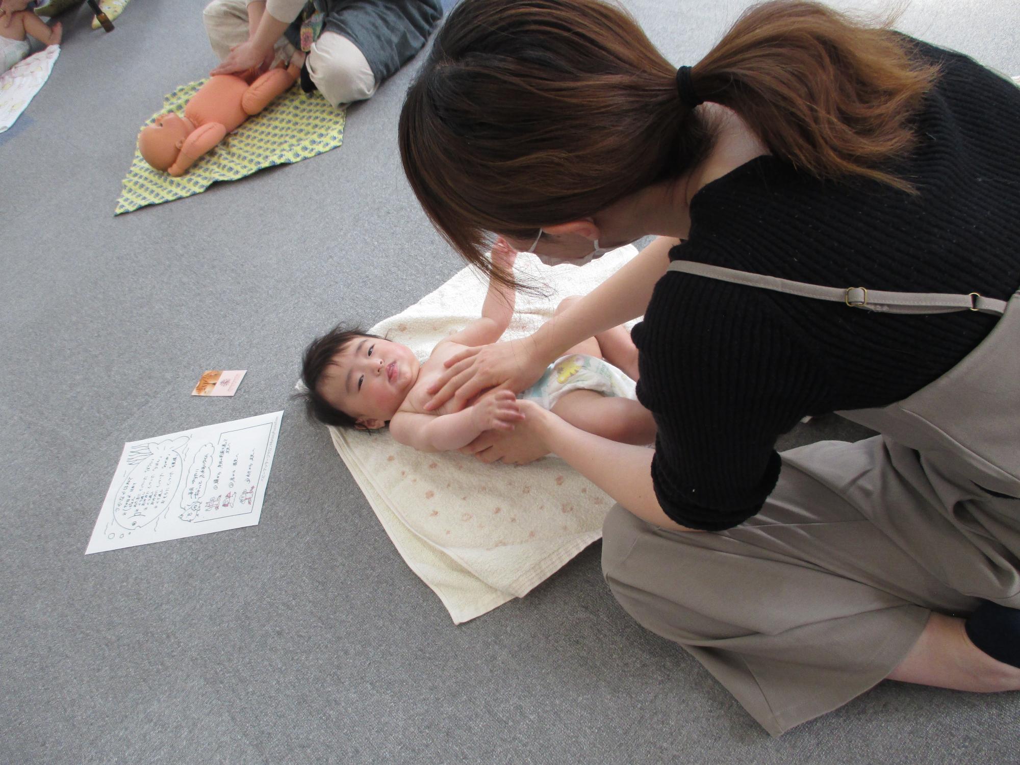 裸であおむけに寝た赤ちゃんの胸、おなかをやさしくなでる母