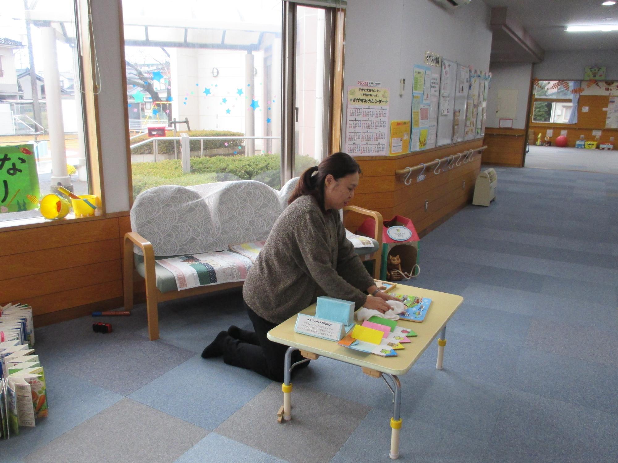 テーブルの上のおもちゃを立ち膝の女性が拭いている