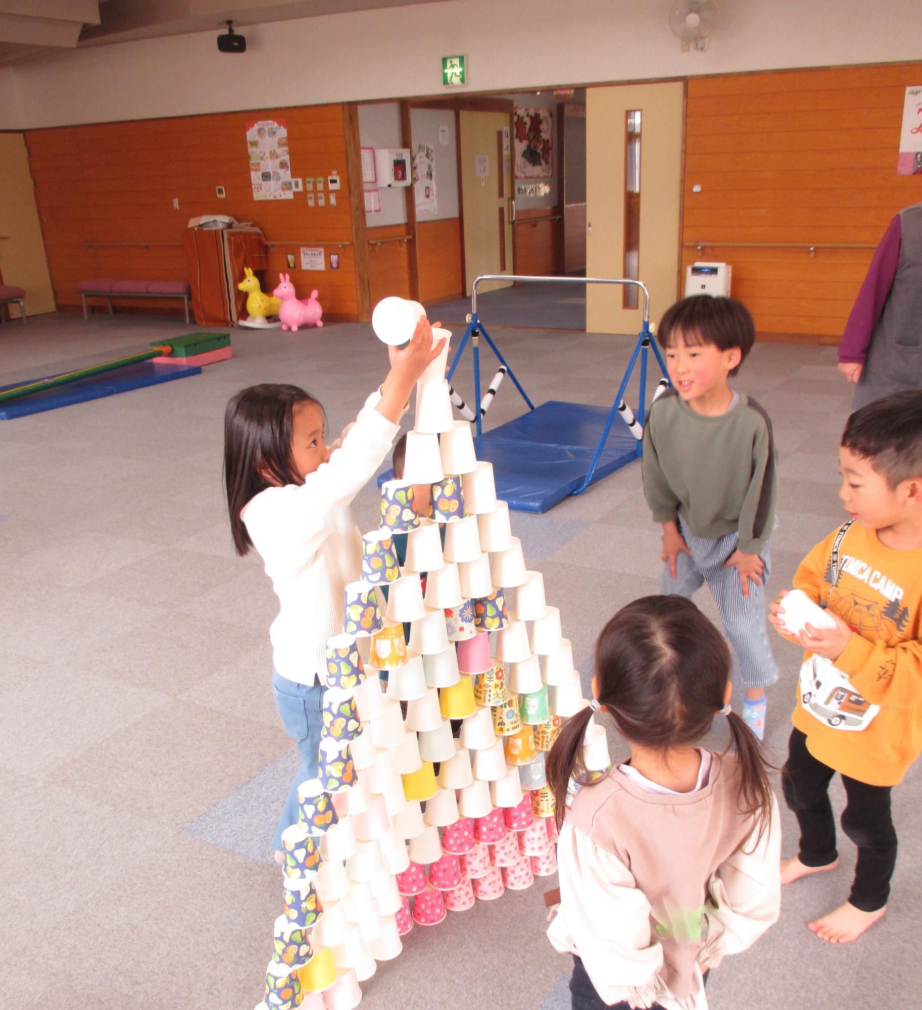 紙コップタワーを積んでいる女の子の周りで3人の子が見ている