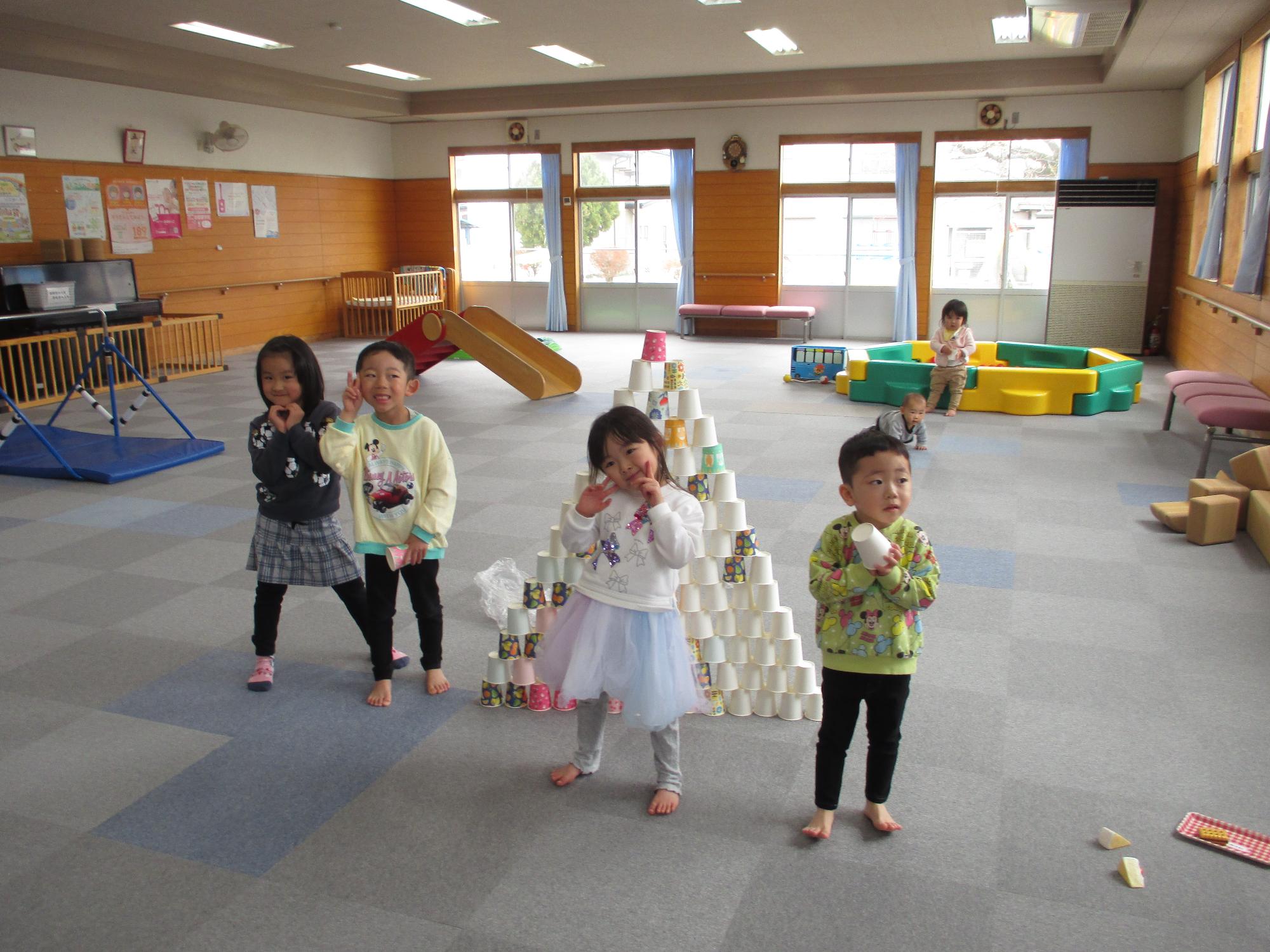 紙コップタワーの前でポーズをとる4人の子ども
