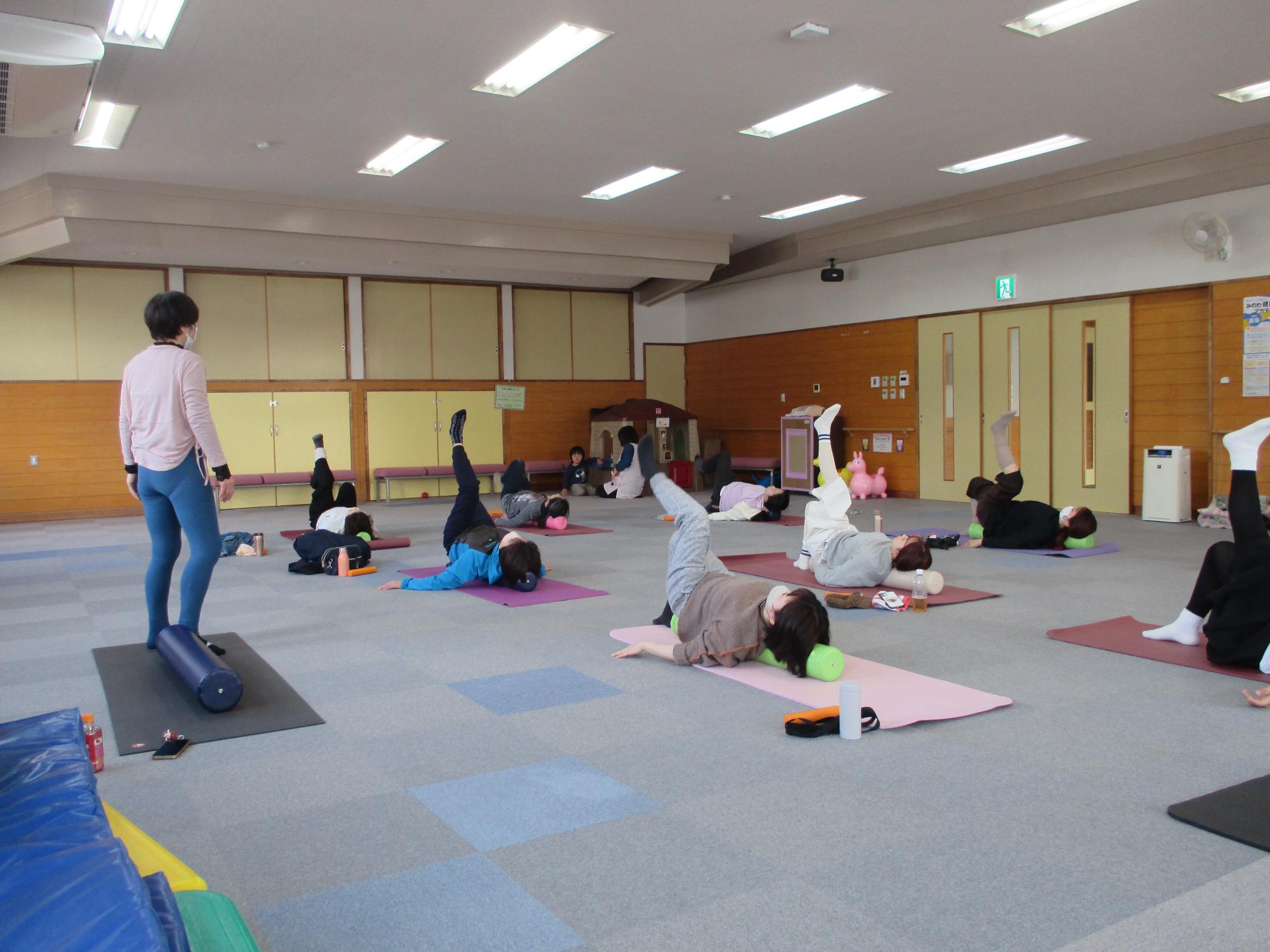 講師が見守る中あおむけに寝た参加者が片足を挙げている