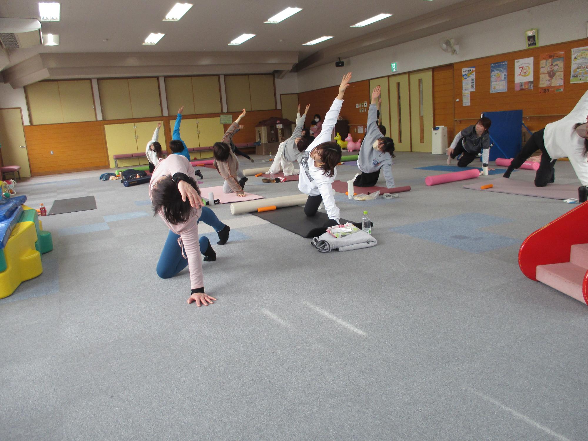 講師を見本に左ひざと左手を床につき右足を伸ばして右手を上にあげている