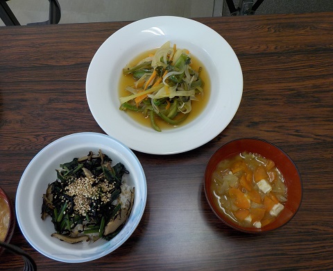ご飯が盛られた茶碗にヒジキや椎茸で作られた料理にゴマが振りかけられ、お椀に豆腐や人参などの野菜が入ったお味噌汁が注がれ、大きなお皿の中にキャベツや人参、ピーマンなどの野菜が細長くカットされ味付けられて完成したおかずが盛り付けられている写真