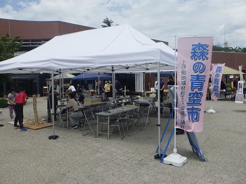 「森の青空市」と書かれたのぼりが立ちテントの下には木でできた積み木のようなものを2人の子供が高く積み上げている写真