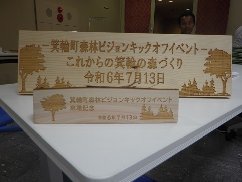 大きさの異なる2枚の木材の看板に両脇に木々が描かれ大きい方は「箕輪町森林ビジョンキックオフイベントこれからの箕輪の森づくり令和6年7月13日」、小さい方は「箕輪町森林ビジョンキックオフイベント来場記念 令和6年7月13日」と書かれている写真