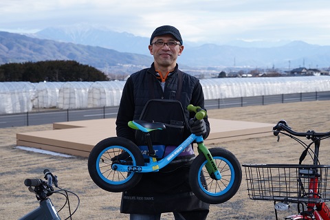 男性が水色の小さなキックバイクを持って立っている写真