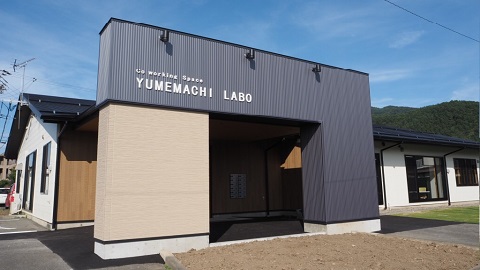 平屋建ての家に大きなグレーを基調とした入口がある箕輪町のコワーキングスペースの外観写真