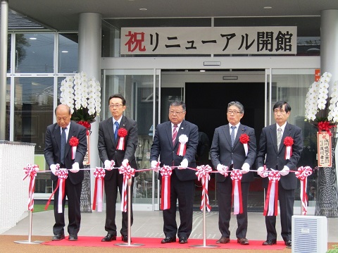 入り口の上に「祝 リニューアル開館」と書かれた幕が貼られ、5名の関係者の方々が横一列に並びテープカットが行われようとしている様子の写真