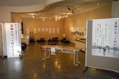 「箕輪の冬って何がある？」と書かれた紙が貼られた展示ホールの壁に写真などが貼られ、ショーケースが設置されている写真