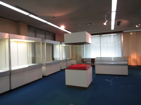 引っ越しの準備が始まり展示物が移動され、壁側や中央に設置されているショーケースだけが部屋に残っている写真