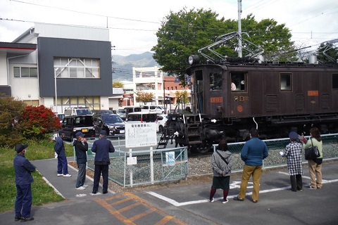 屋外に展示されている電気機関車を、4名の作業員の方や参加者が見ている写真
