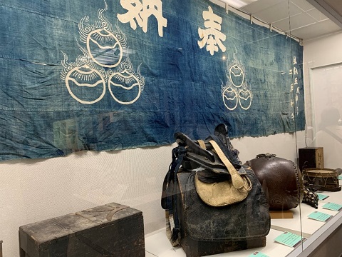 ショーケース内に展示された、奉納と書かれた横長で大きな旗や奉納品などの写真