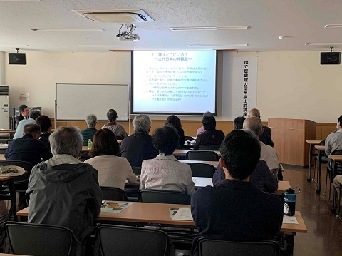 前方に設置されたスクリーンに資料が映し出され、左前に座っている櫻井氏の話を席に座った参加者が聞いている後ろ姿の写真