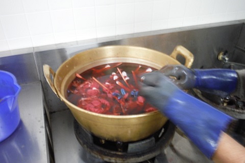 大きな鍋の中に赤色のもみじから抽出して染まったお湯の中に、割り箸と一緒に縛った布が入っている写真