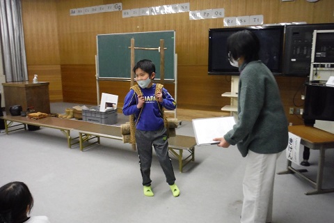 緑色の服を着た女性職員と背負子を背負った男児の写真