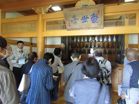 観音堂に安置されている32体の観音像の左側に立つ柴館長の話を、参加者が熱心に聞いている後ろ姿の写真