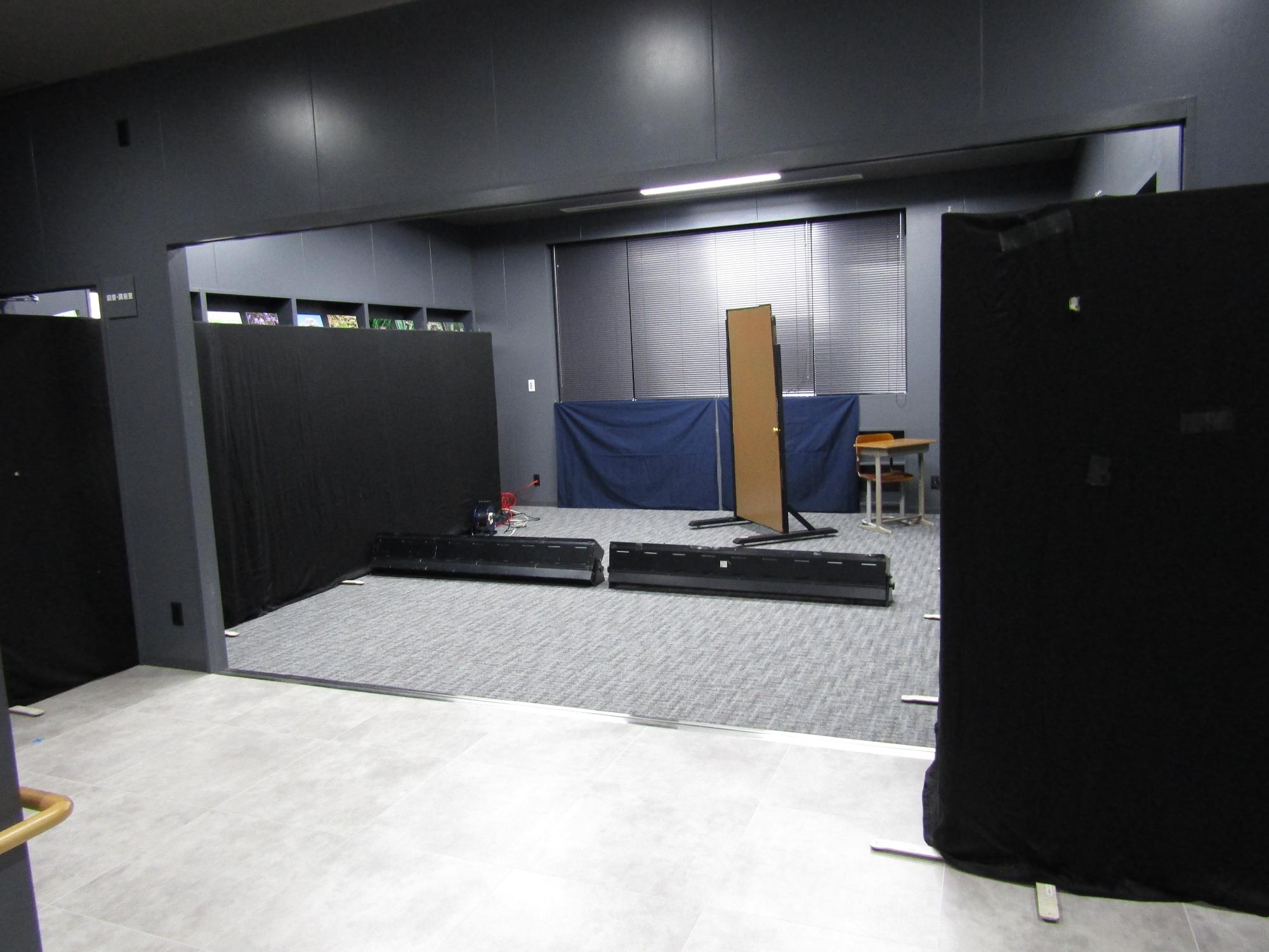 図書講座室を暗幕をかけたパーテンションで区切り、舞台を舞台袖を分けている。中央にはドアの大道具とフットライトが置いてある。