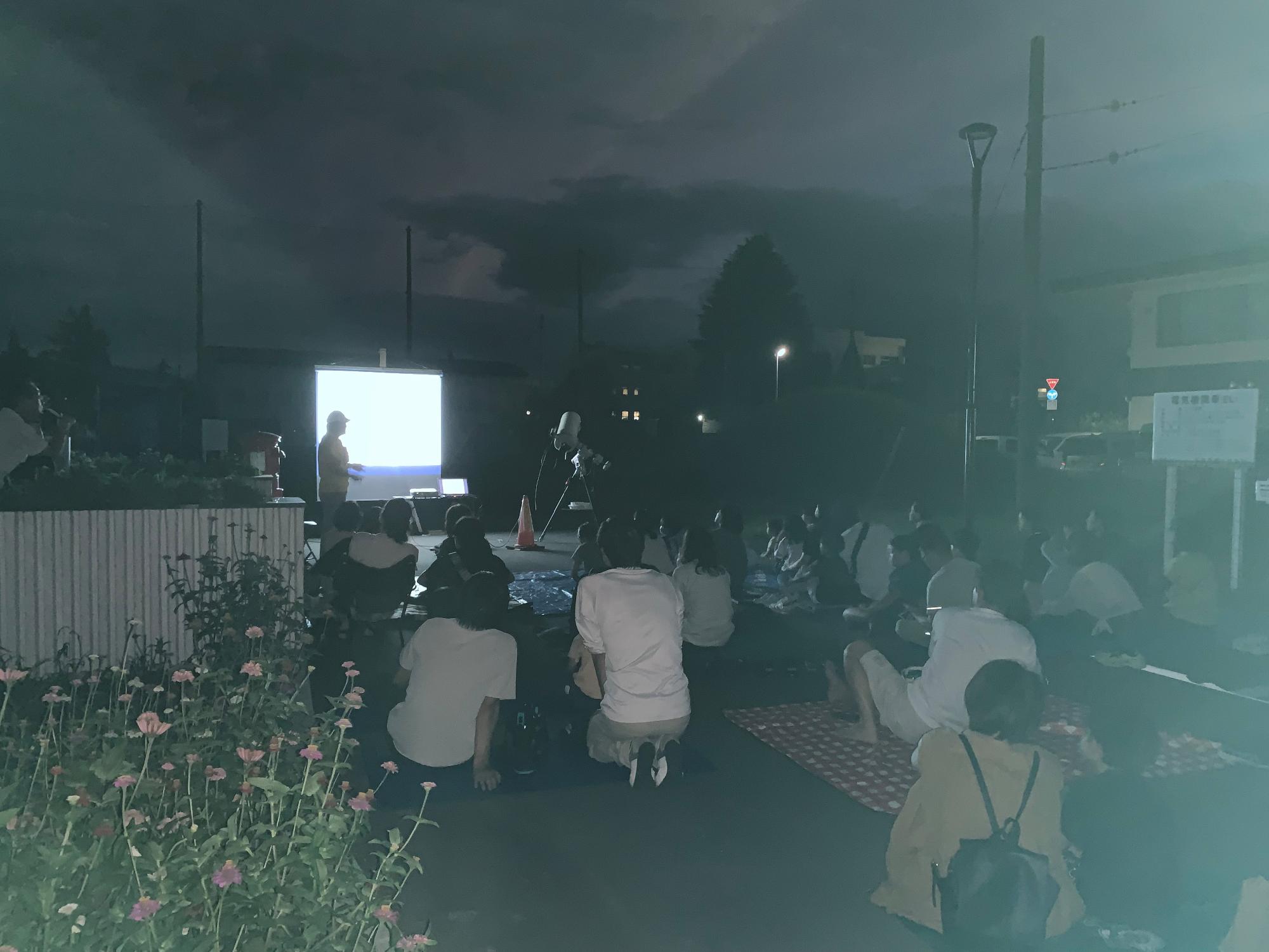 スクリーンの前で講師が説明していて、参加者は座って話を聞いている