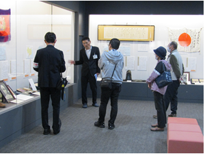 展示解説で、学芸員の話に聞き入る参加者