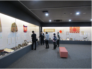 展示ケースの前で展示の解説をする学芸員と、話を聞く参加者の皆さん