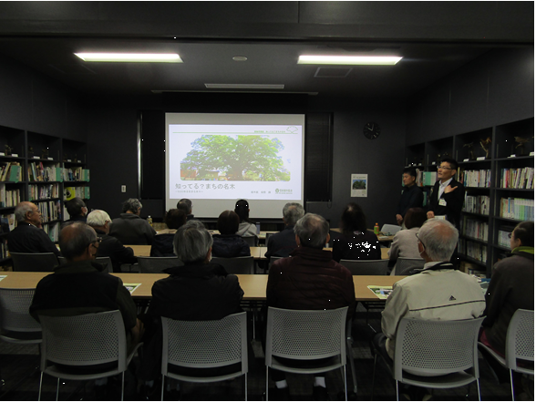 博物館の図書講座室で司会者が前に立って話し、参加者が座って話を聞いている