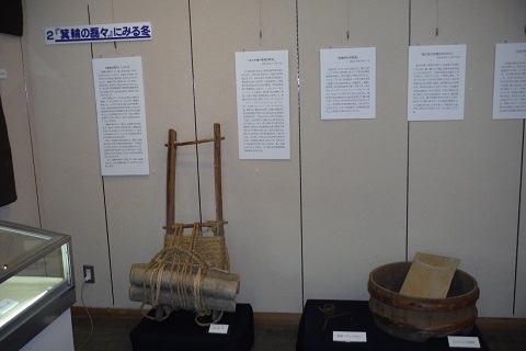 資料が貼られた壁の下に、背負子や洗濯板などの生活道具が展示されている写真