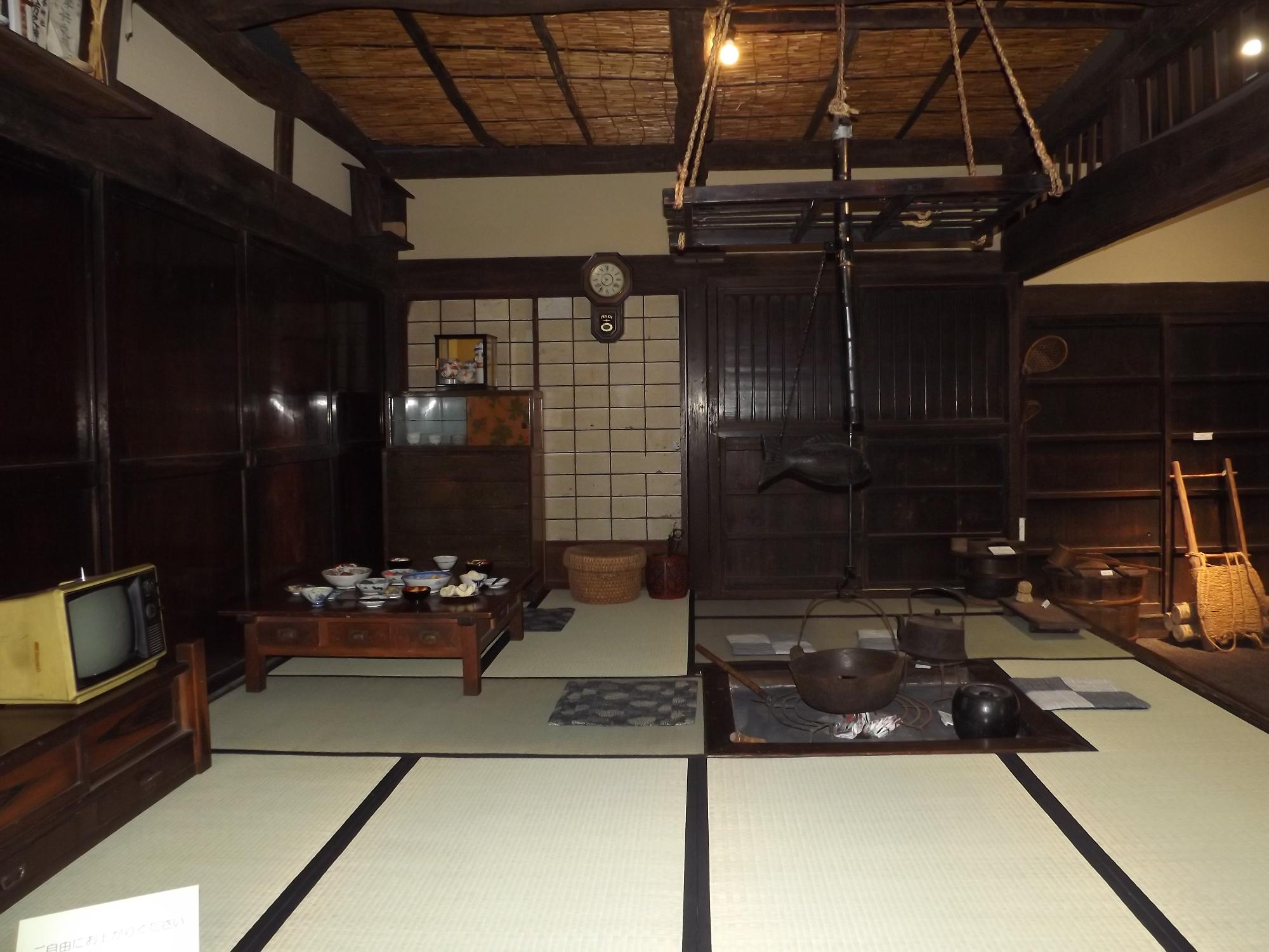 真ん中に囲炉裏があり、畳が敷かれている。奥には大きな棚があり、囲炉裏の左には食卓を再現したテーブルがある