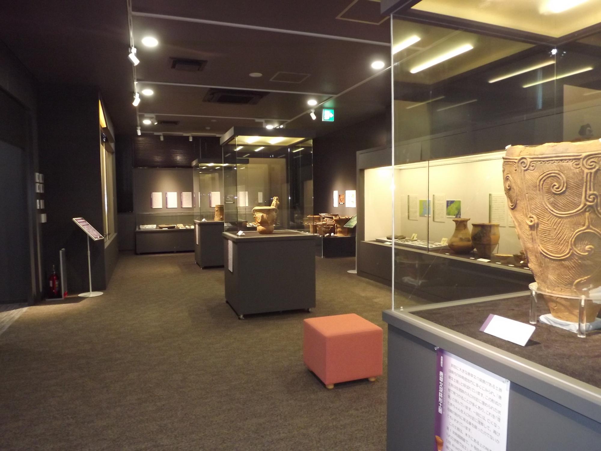 黒色の壁面の歴史展示室。独立展示ケースには縄文土器が1つずつ展示。右側の展示ケースには弥生土器。奥には縄文土器がオープン展示してある