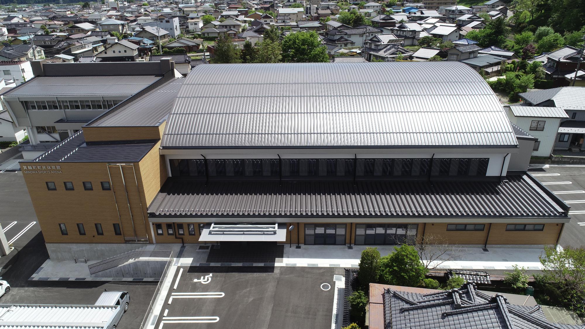 湾曲した灰色の屋根で、木目調の外壁の箕輪町町民体育館の建物外観の写真
