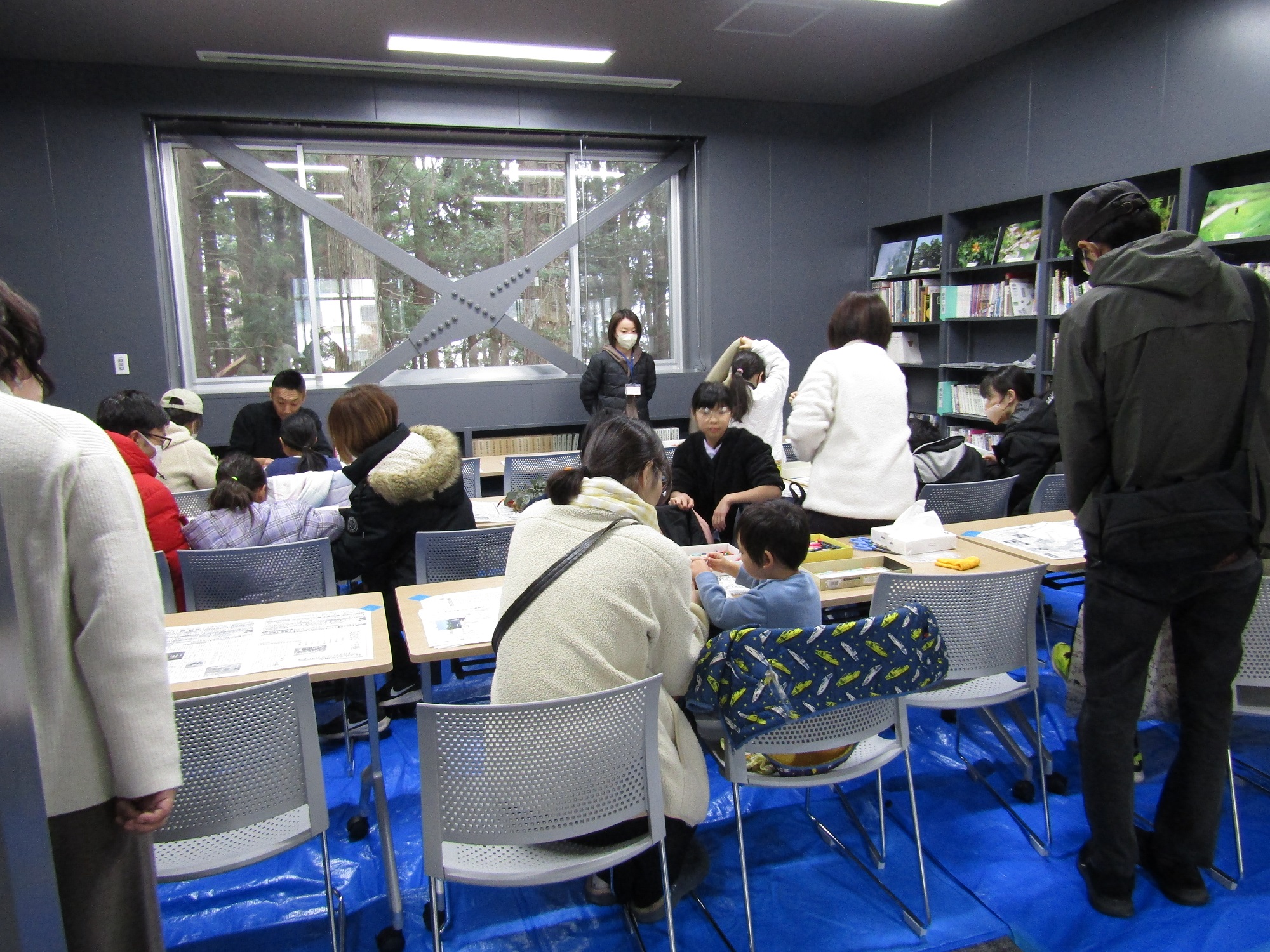 図書講座室の床にブルーシートを敷き、テーブルを並べてある。その机に向かい、椅子に座りながら管玉を作っている。親子連れが多い。