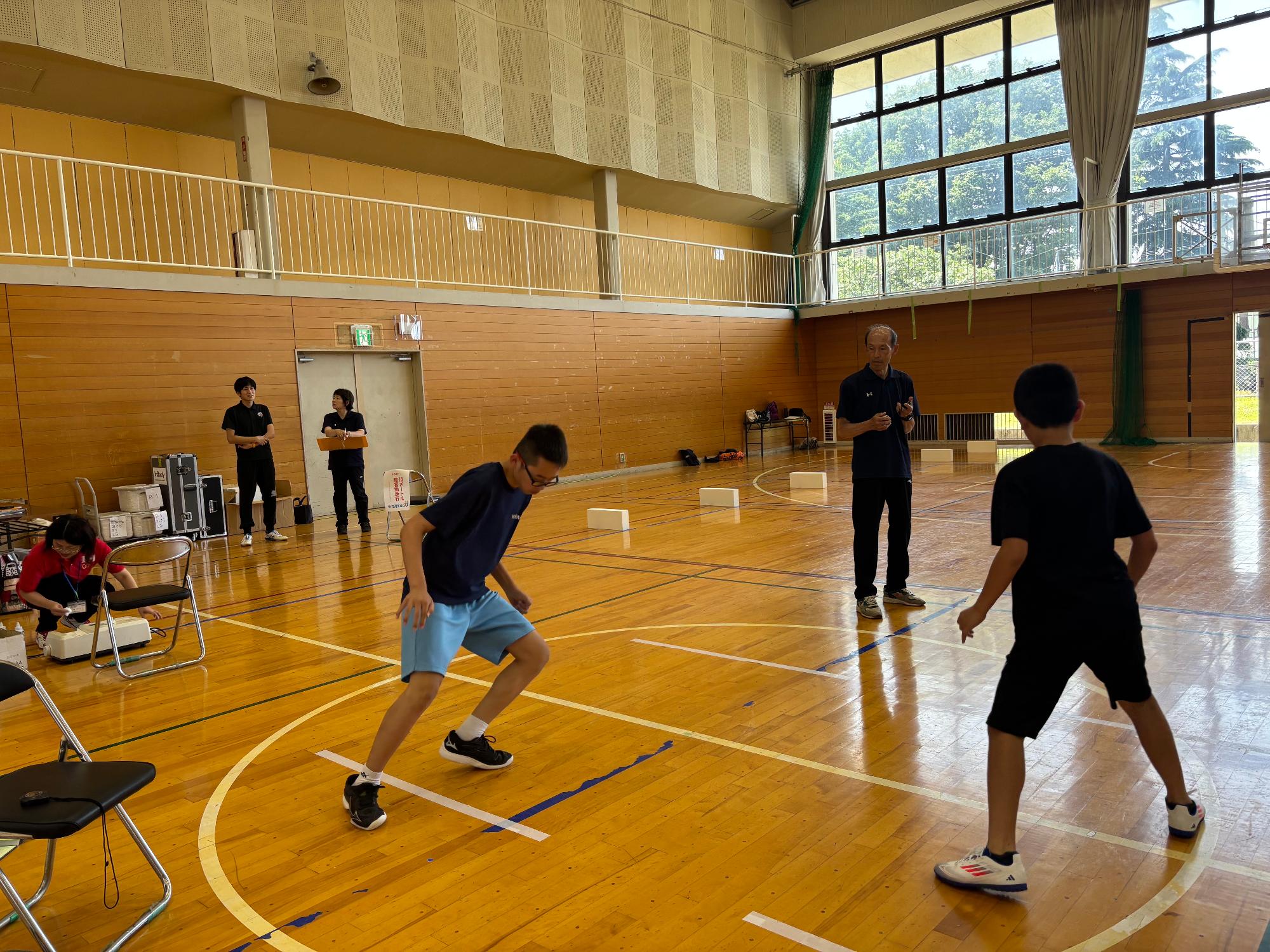 体育館内で反復横跳びをする学生の写真