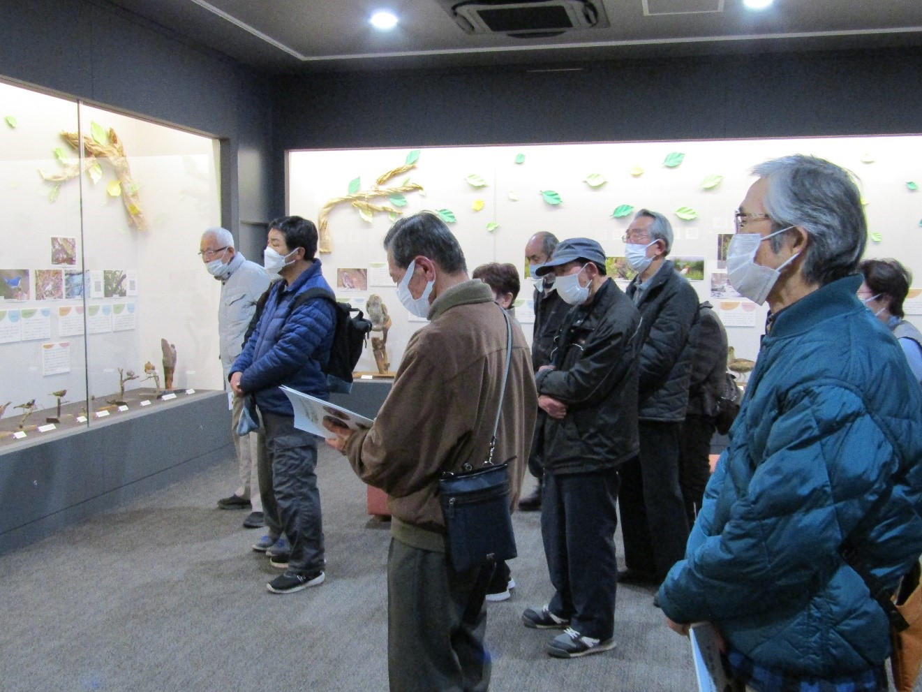 展示解説で説明を聞く参加者。ほとんどが年配の男性。