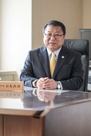町長席の机の上に両手を揃えて置いて座っている白鳥町長の写真