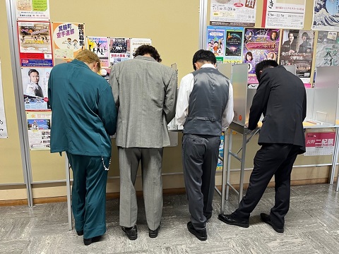 投票記載台に4人の男性が記載している所を後ろから写した写真