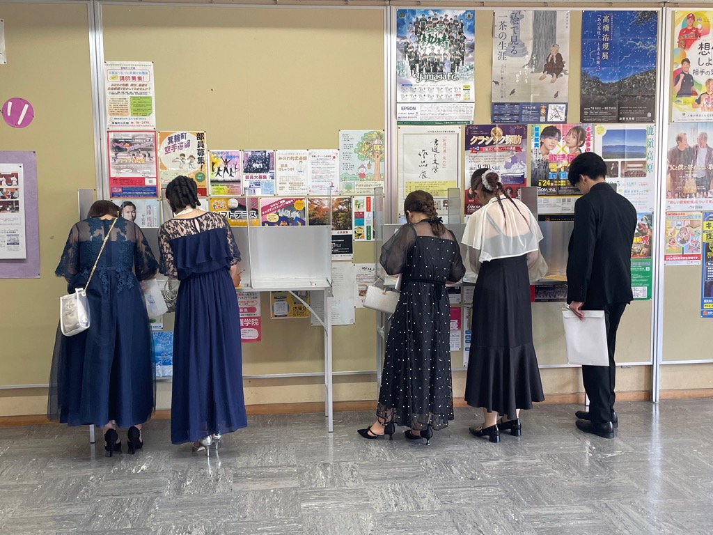 記載台で5人の男女が記載している様子を後ろから撮影したもの