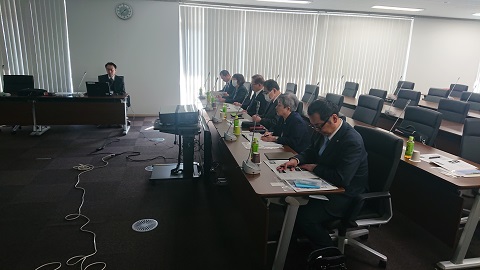照明を落とした室内で、参加者が横一列に並んで座っている委員会の様子の写真