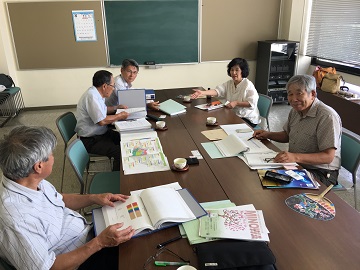 会議室で各々資料を広げて話し合いをしている5名の関係者の写真