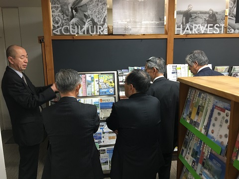 表紙が見えるようにパンフレットが並べられているコーナーで小山所長から説明を受けている様子の写真
